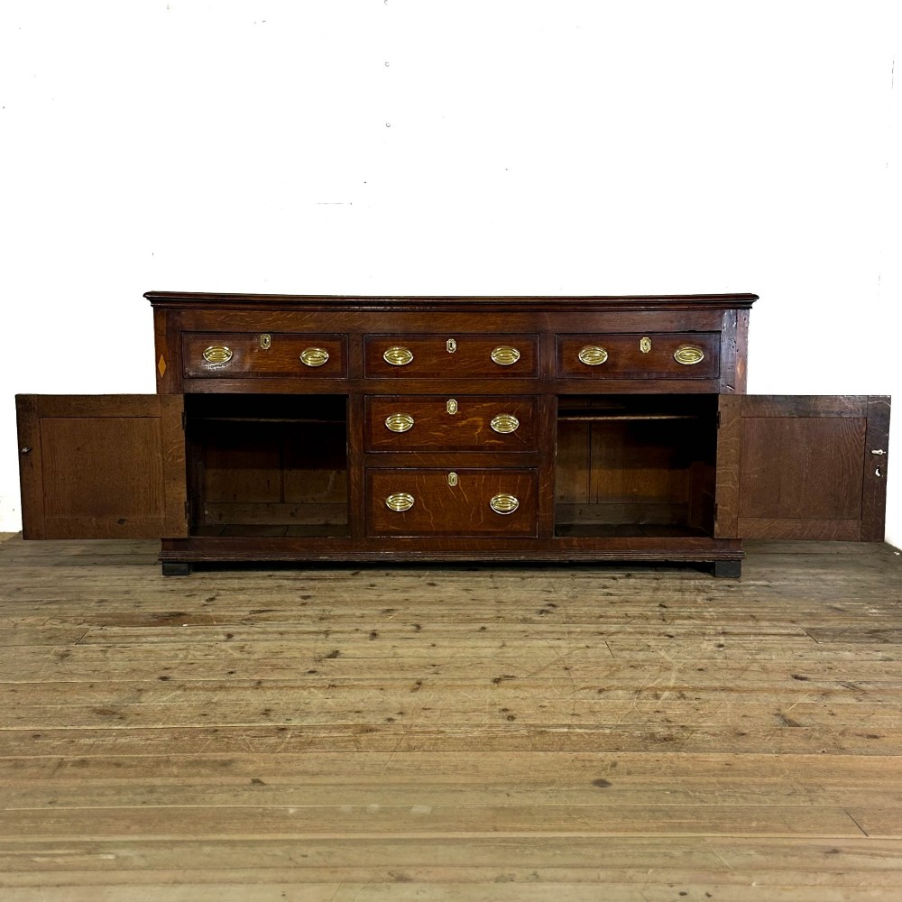 An antique Georgian oak dresser base featuring brass oval drop handles, panelled cupboard doors, central drawers, and geometric diamond inlay. View VIII