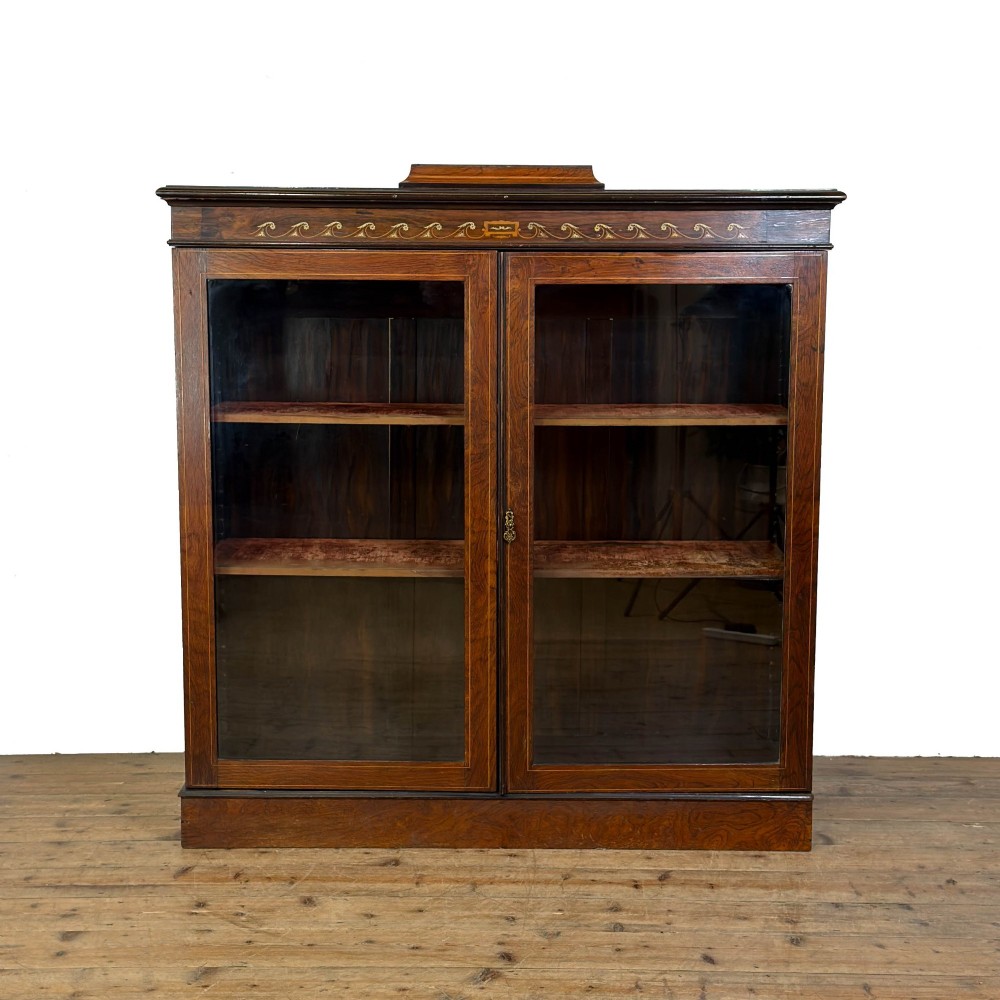 An Edwardian dark mahogany display cabinet featuring two glazed doors, satinwood scroll marquetry along the top frieze, and internal wooden shelves.