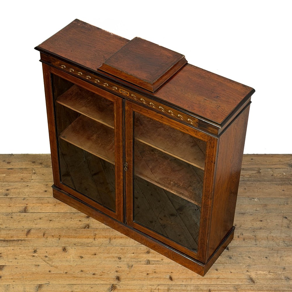 An Edwardian dark mahogany display cabinet featuring two glazed doors, satinwood scroll marquetry along the top frieze, and internal wooden shelves. View VI