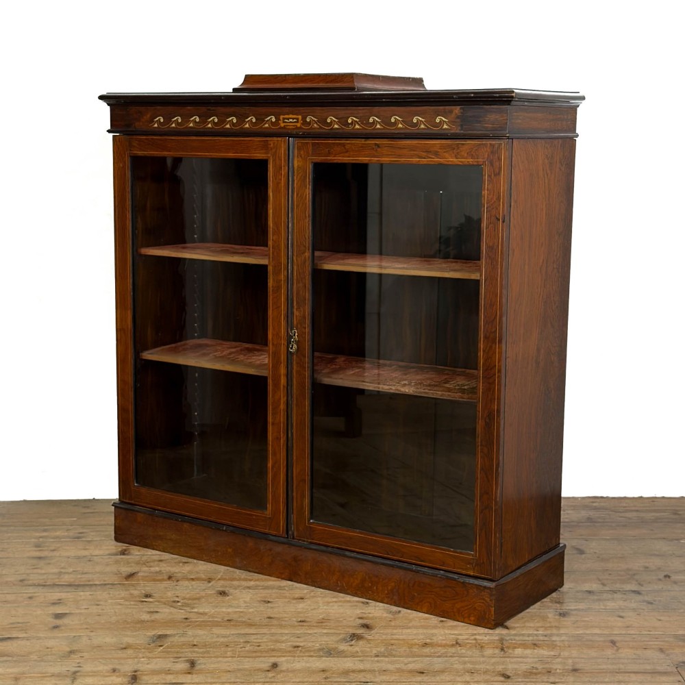 An Edwardian dark mahogany display cabinet featuring two glazed doors, satinwood scroll marquetry along the top frieze, and internal wooden shelves. View IX