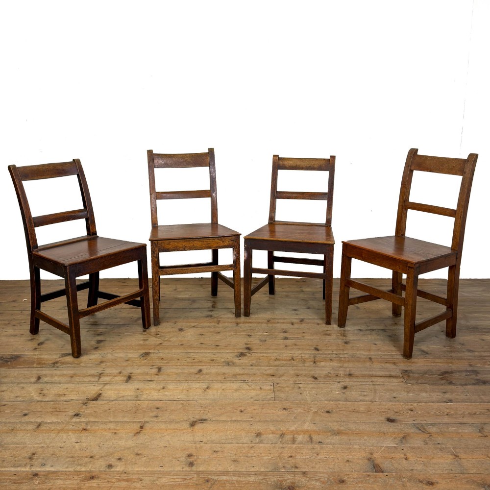 A harlequin set of four dark brown oak country dining chairs featuring horizontal ladder backs and solid wood seats on square legs.
