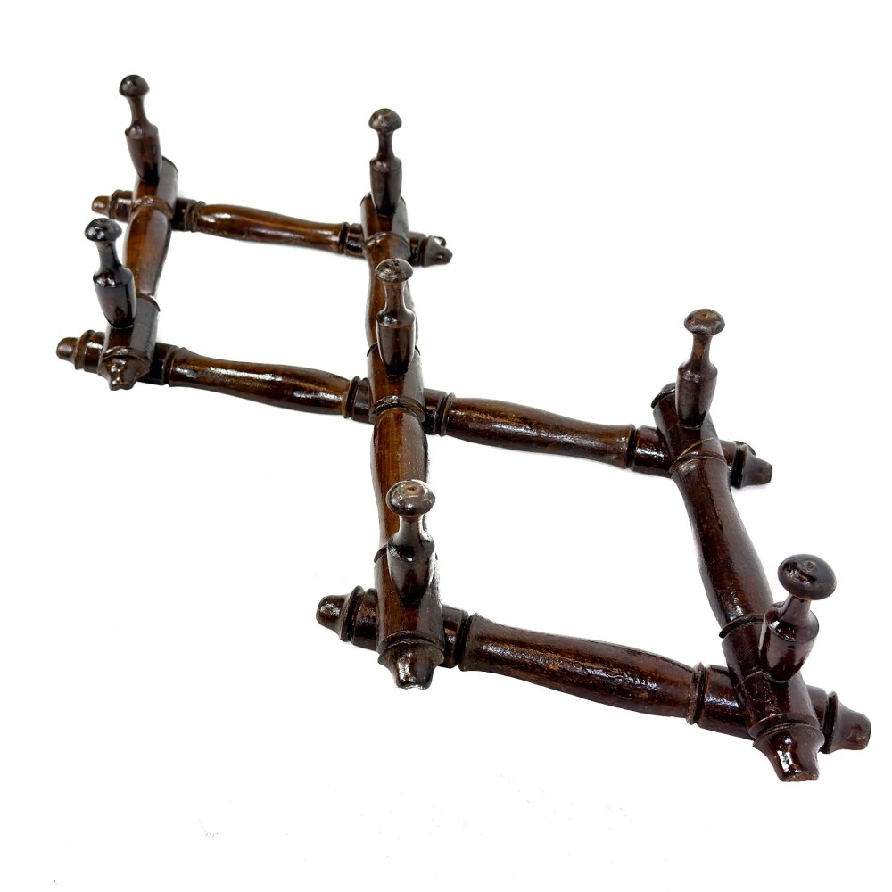 A dark brown wooden extending accordion coat rack with turned pegs arranged in a diamond lattice frame. View VII