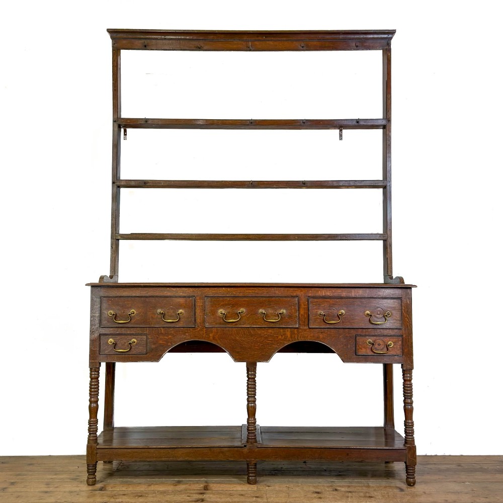 A 19th-century dark oak Welsh potboard dresser featuring an open three-shelf plate rack resting on a five-drawer base with turned legs.