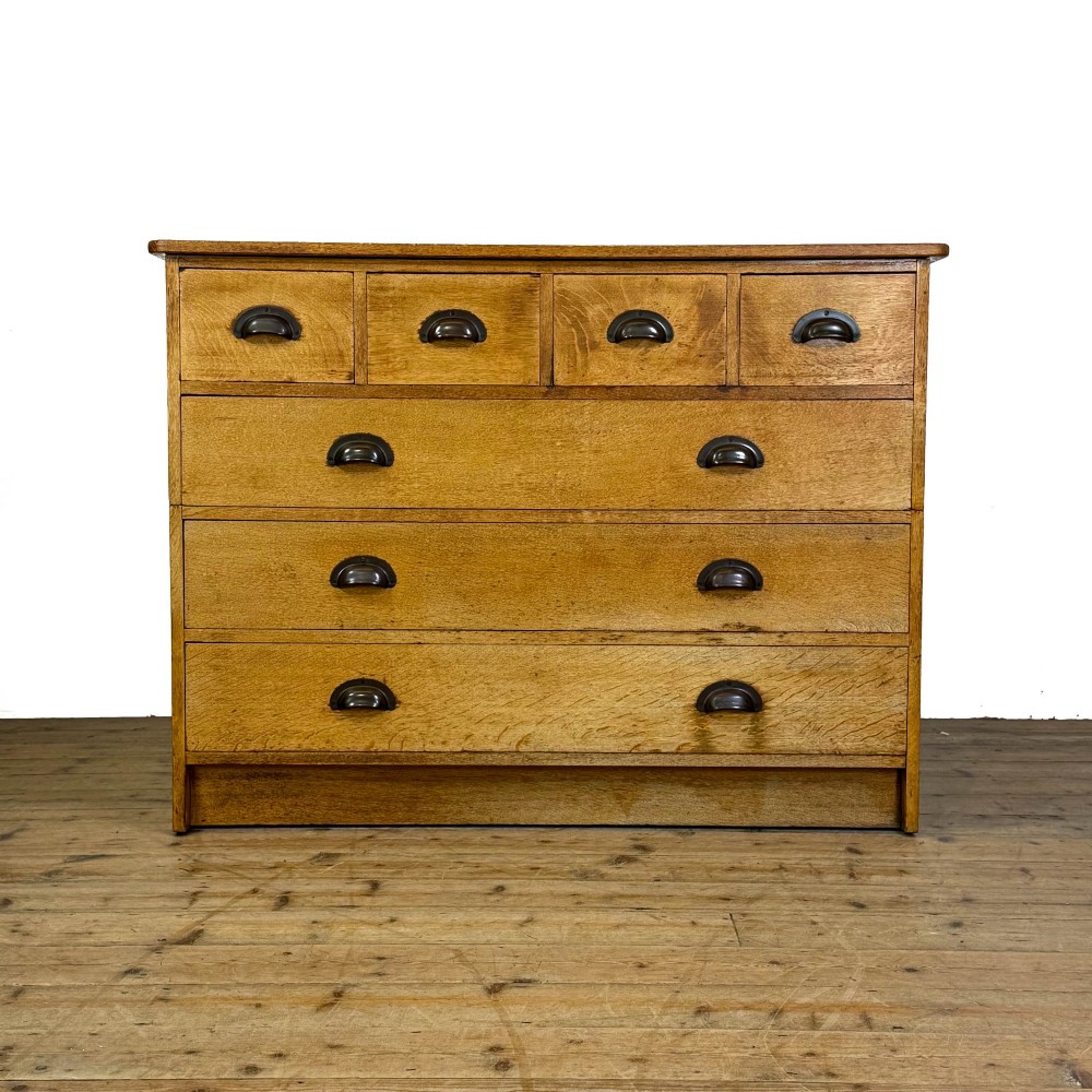 A vintage pale oak chest of drawers featuring four small top drawers above three wide drawers, fitted with dark metal cup handles.