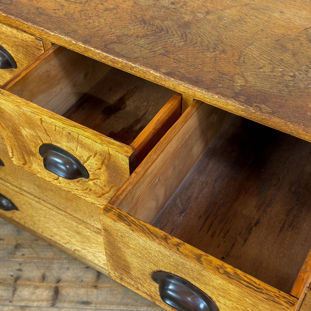 A vintage pale oak chest of drawers featuring four small top drawers above three wide drawers, fitted with dark metal cup handles. View VIII