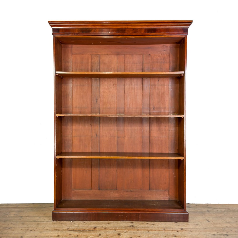 A large antique open mahogany bookcase with a moulded top cornice, multiple storage shelves, and vertical panelled timber backing.