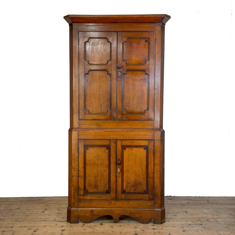 A two-tier freestanding Georgian oak corner cabinet with panelled double doors, brass keyhole escutcheons, and a moulded cornice.