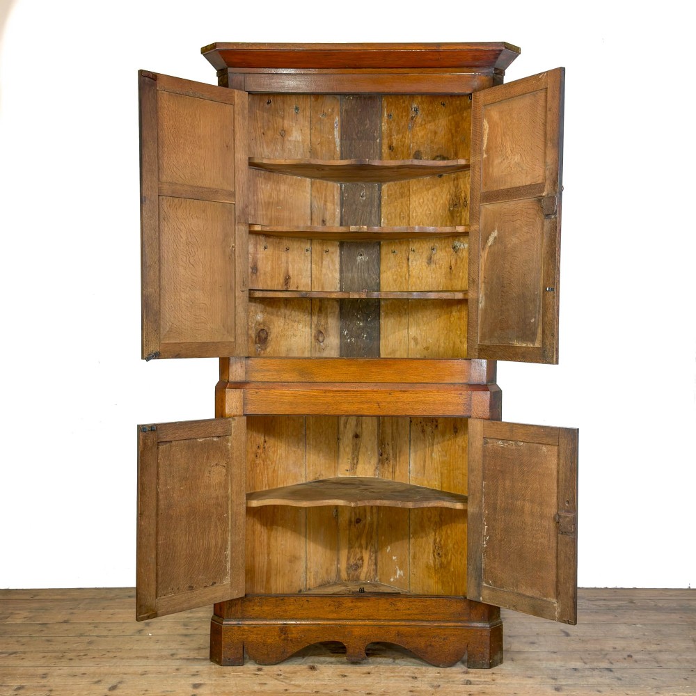 A two-tier freestanding Georgian oak corner cabinet with panelled double doors, brass keyhole escutcheons, and a moulded cornice. View II