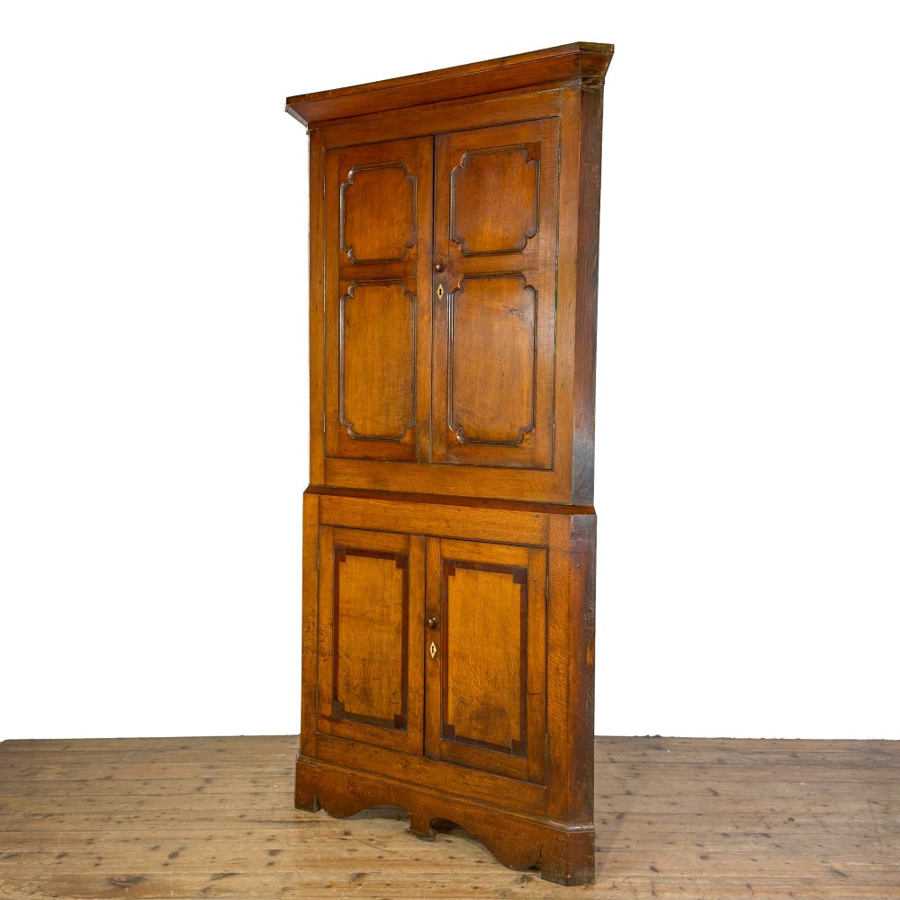 A two-tier freestanding Georgian oak corner cabinet with panelled double doors, brass keyhole escutcheons, and a moulded cornice. View IV