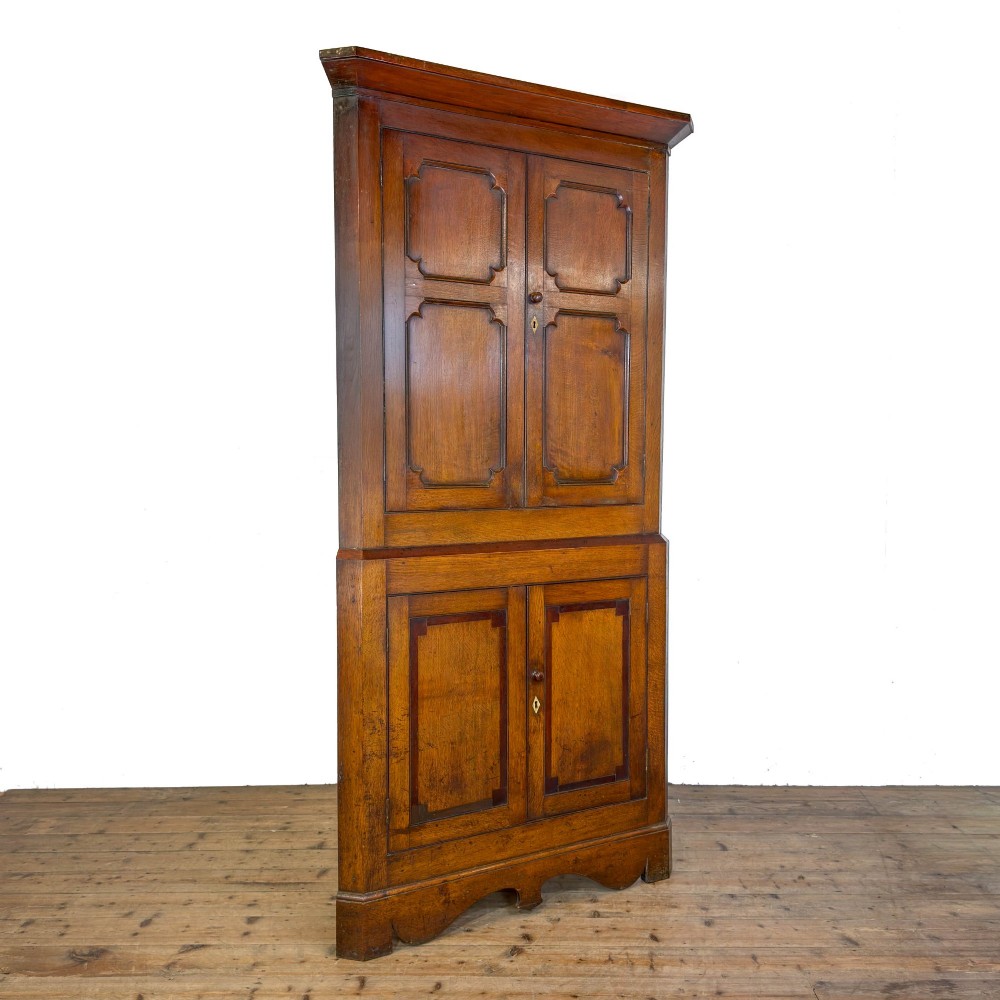 A two-tier freestanding Georgian oak corner cabinet with panelled double doors, brass keyhole escutcheons, and a moulded cornice. View VI