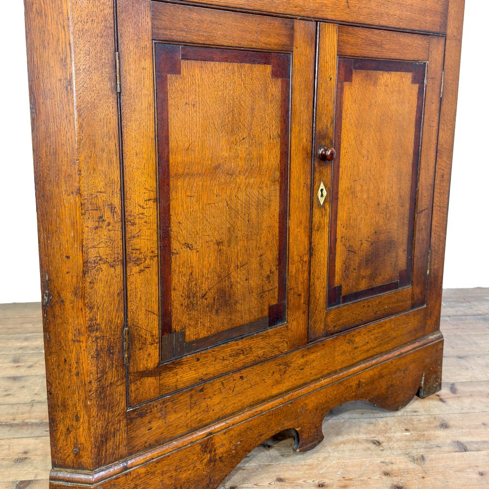 A two-tier freestanding Georgian oak corner cabinet with panelled double doors, brass keyhole escutcheons, and a moulded cornice. View VII