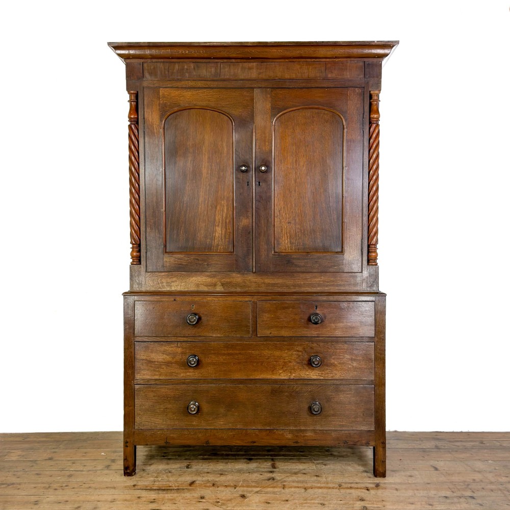 A 19th-century oak linen press featuring a two-door upper cupboard flanked by barley twist columns above a chest of drawers.