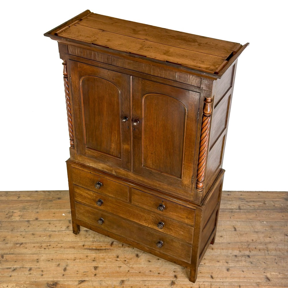 A 19th-century oak linen press featuring a two-door upper cupboard flanked by barley twist columns above a chest of drawers. View VI