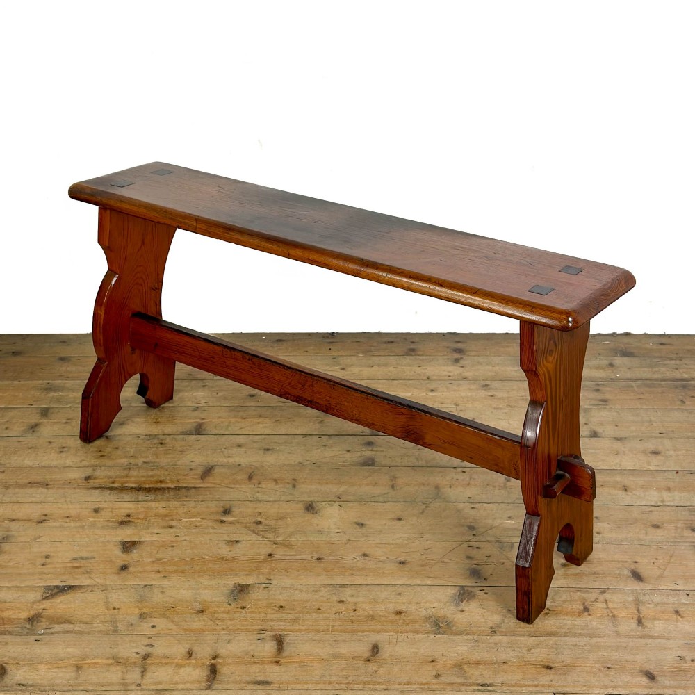 An antique pine bench featuring a long plank top, shaped trestle end supports, and a lower wooden stretcher rail. View II