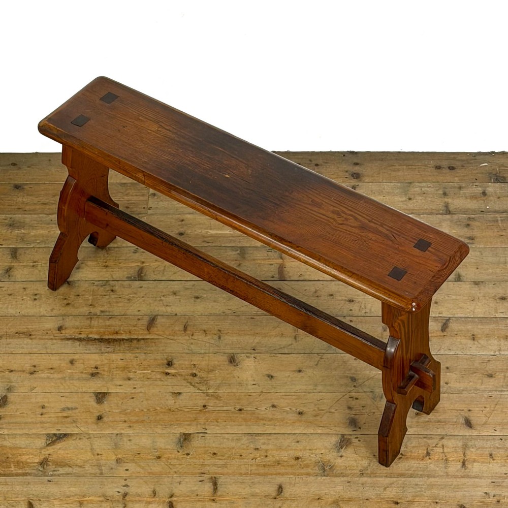 An antique pine bench featuring a long plank top, shaped trestle end supports, and a lower wooden stretcher rail. View III