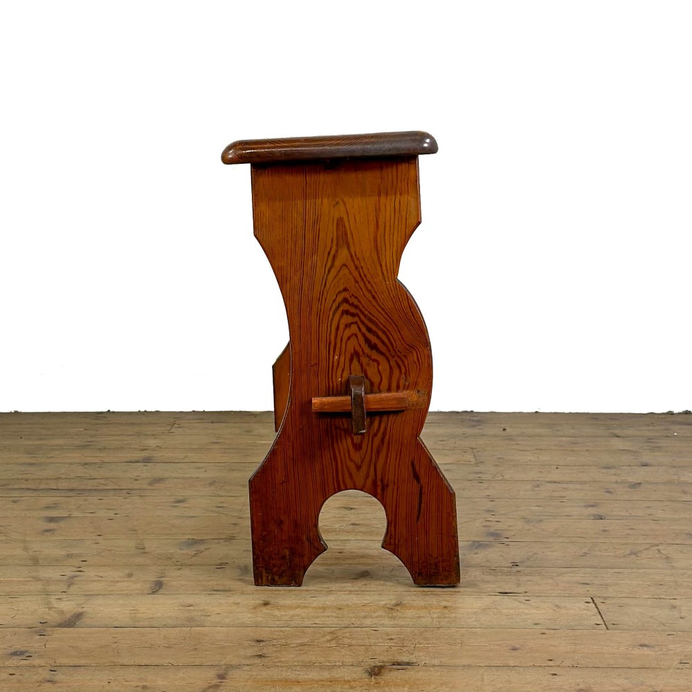 An antique pine bench featuring a long plank top, shaped trestle end supports, and a lower wooden stretcher rail. View VII