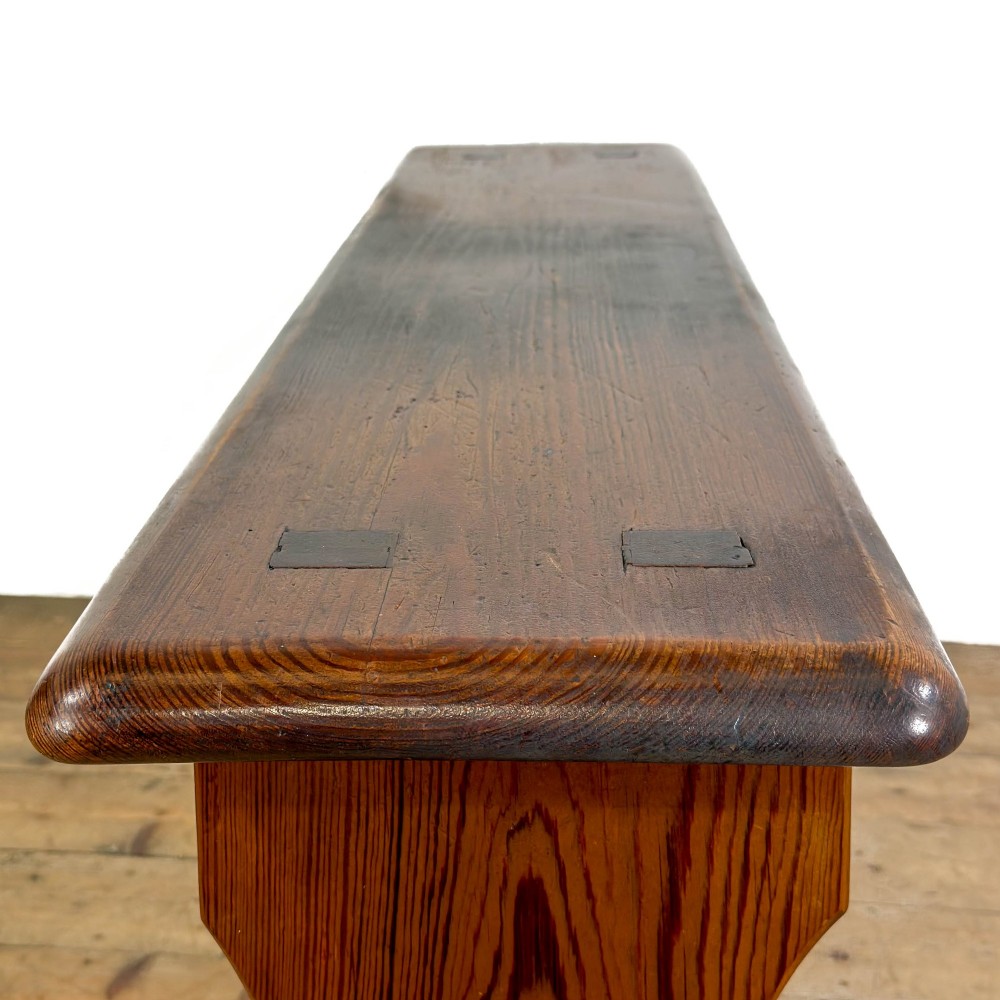 An antique pine bench featuring a long plank top, shaped trestle end supports, and a lower wooden stretcher rail. View VIII
