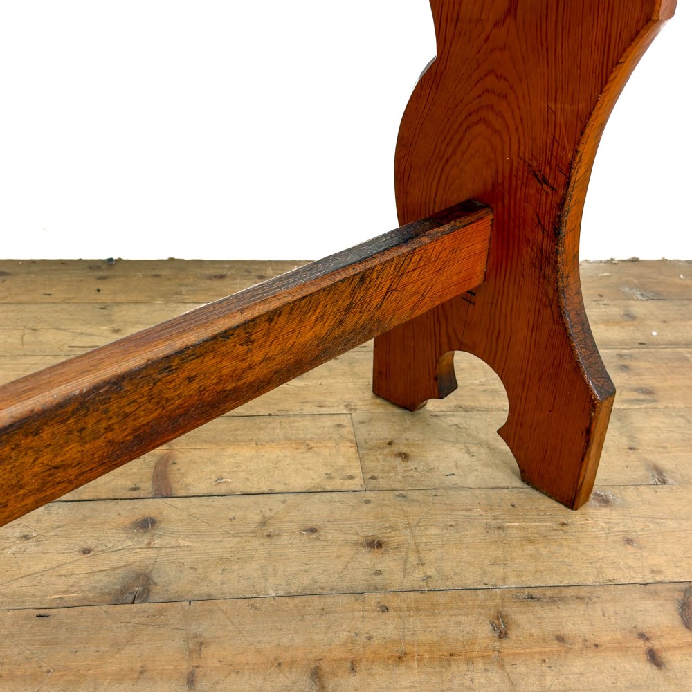 An antique pine bench featuring a long plank top, shaped trestle end supports, and a lower wooden stretcher rail. View IX
