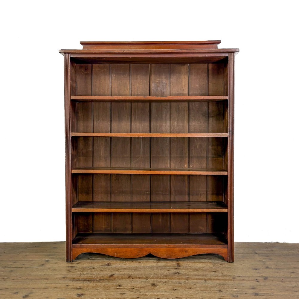 A tall 19th-century open wooden bookcase featuring five fixed shelves, fluted side stiles, a stepped pediment, and a shaped apron base.