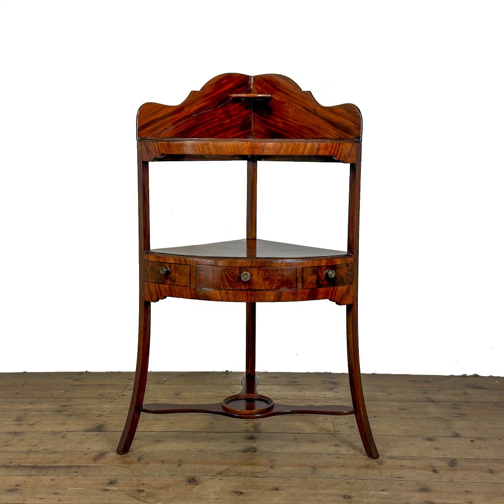 A Georgian mahogany corner washstand featuring a shaped splashback, middle drawer section with brass knobs, and curved splayed legs.