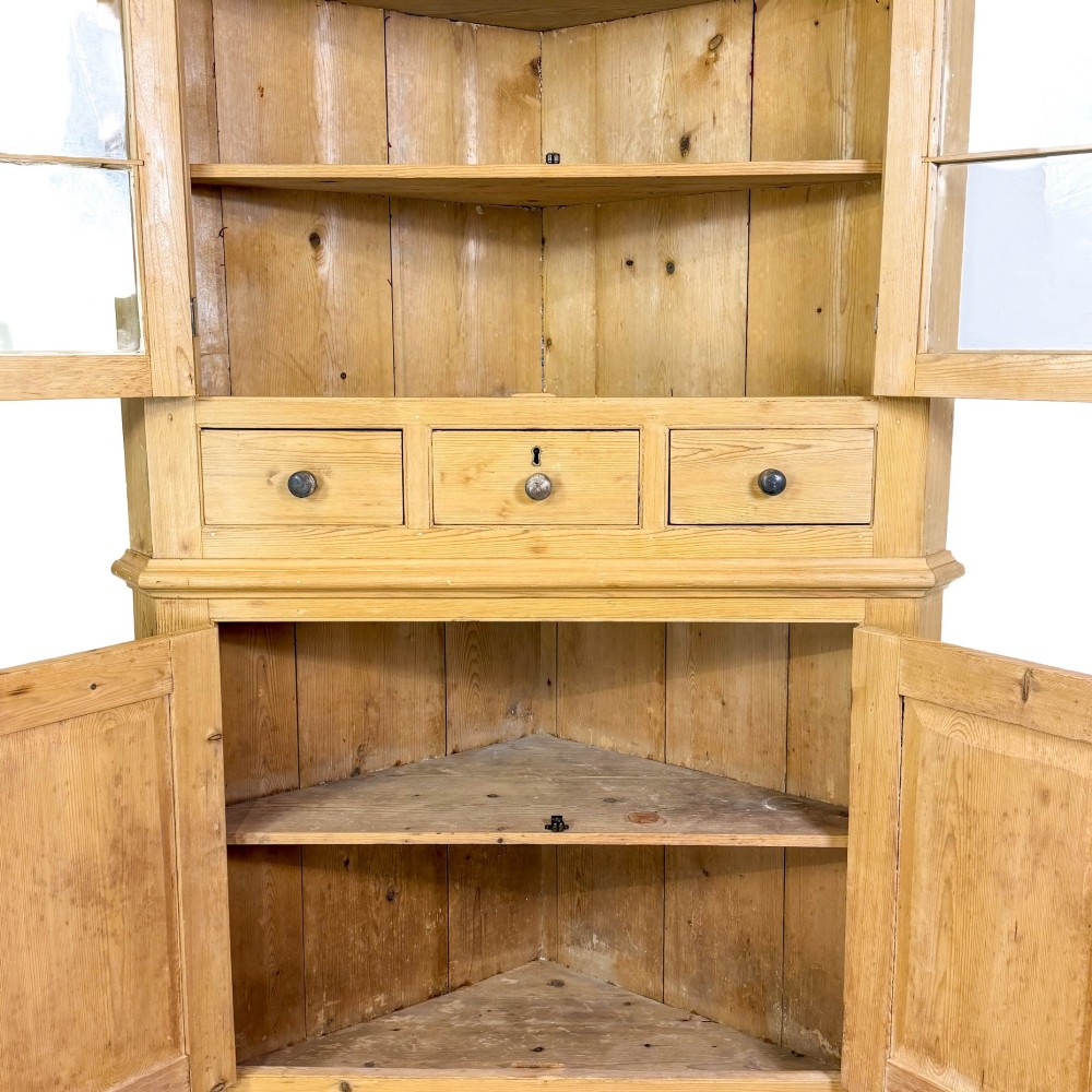 An antique stripped pine corner cabinet featuring arched glazed doors on the upper section, three drawers, and twin panelled cupboard doors below. View III