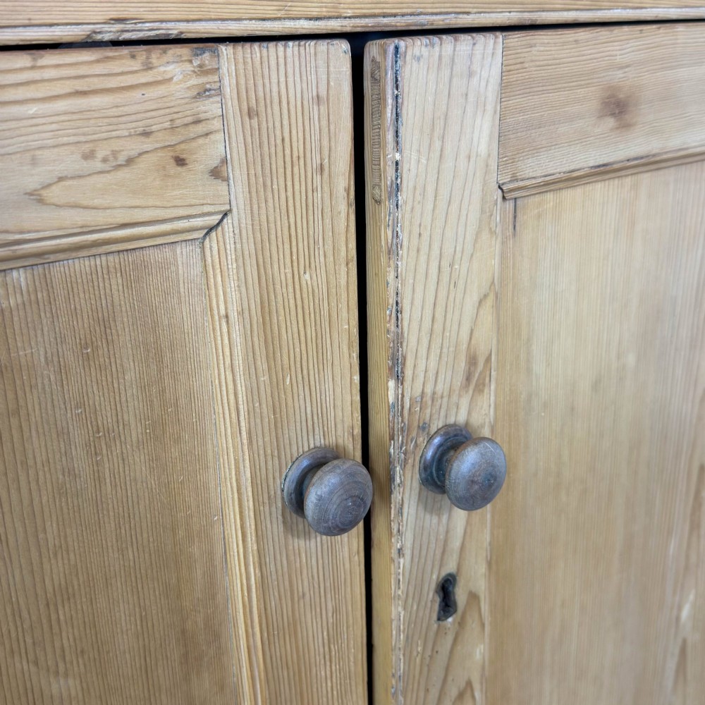 An antique stripped pine corner cabinet featuring arched glazed doors on the upper section, three drawers, and twin panelled cupboard doors below. View V