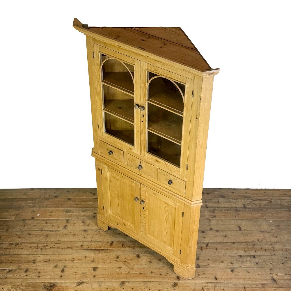 An antique stripped pine corner cabinet featuring arched glazed doors on the upper section, three drawers, and twin panelled cupboard doors below. View VI