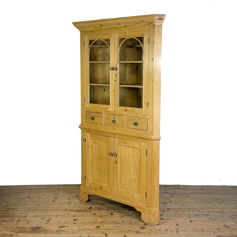 An antique stripped pine corner cabinet featuring arched glazed doors on the upper section, three drawers, and twin panelled cupboard doors below. View VIII