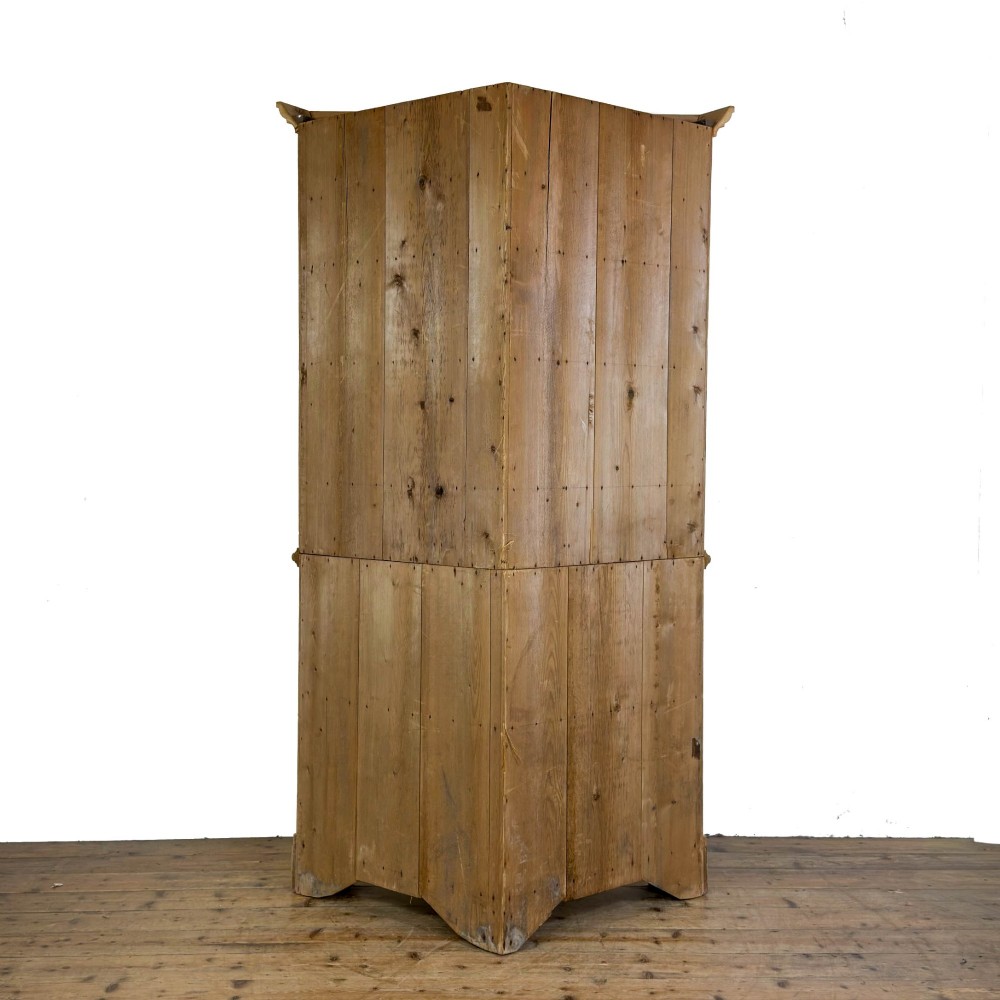 An antique stripped pine corner cabinet featuring arched glazed doors on the upper section, three drawers, and twin panelled cupboard doors below. View X
