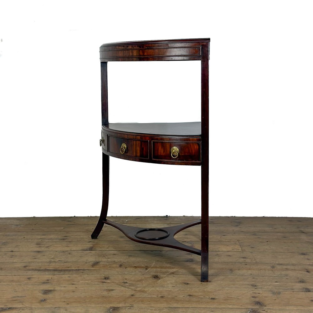 A Georgian dark mahogany triangular corner washstand featuring a smooth top shelf, a middle tier with three drawer fronts and brass ring handles, and slender legs connected by a lower stretcher. View II
