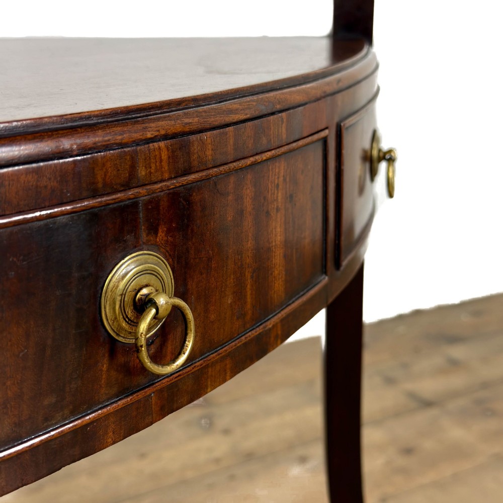 A Georgian dark mahogany triangular corner washstand featuring a smooth top shelf, a middle tier with three drawer fronts and brass ring handles, and slender legs connected by a lower stretcher. View VII