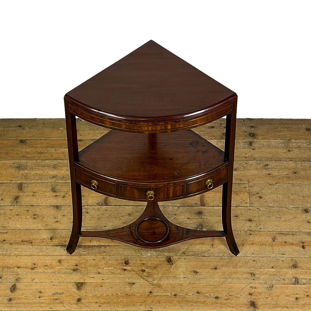 A Georgian dark mahogany triangular corner washstand featuring a smooth top shelf, a middle tier with three drawer fronts and brass ring handles, and slender legs connected by a lower stretcher. View IX