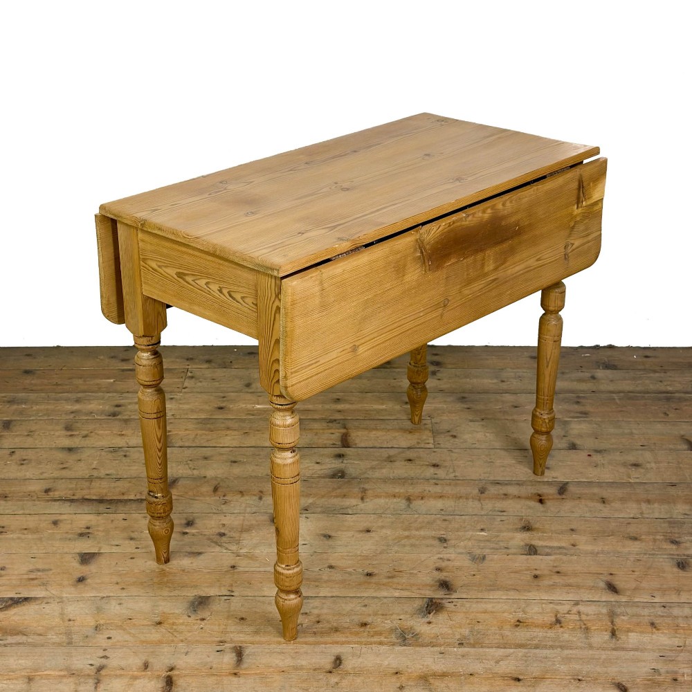 A pine drop leaf kitchen table featuring turned legs and hinged side panels that fold down.