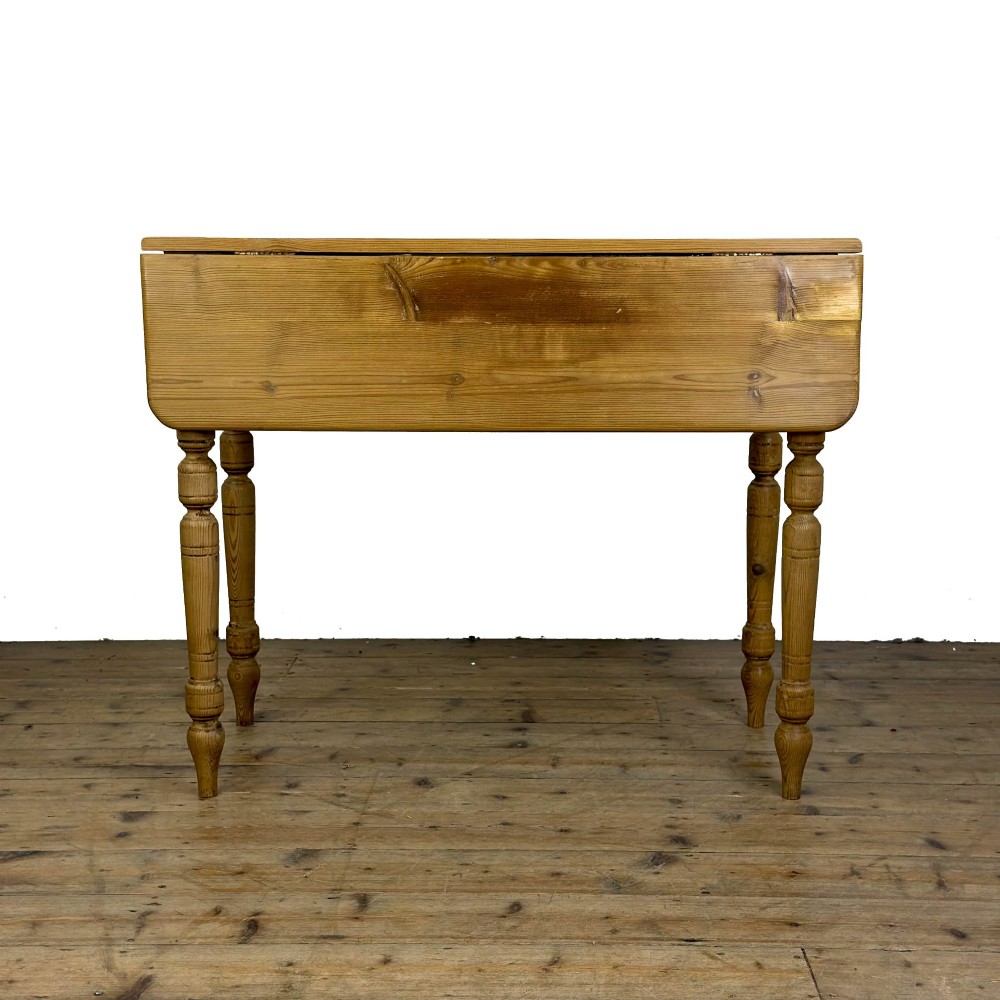 A pine drop leaf kitchen table featuring turned legs and hinged side panels that fold down. View V