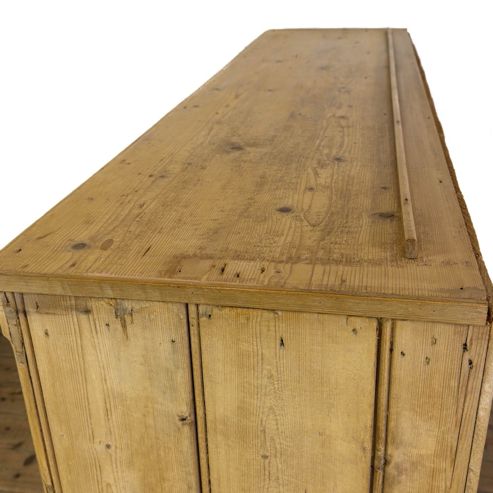 A Victorian pine dresser base with three frieze drawers, ceramic drawer knobs, two panelled cupboard doors, and a central open shelving recess. View VII