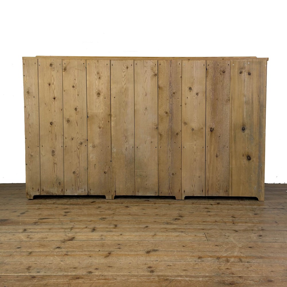 A Victorian pine dresser base with three frieze drawers, ceramic drawer knobs, two panelled cupboard doors, and a central open shelving recess. View VIII