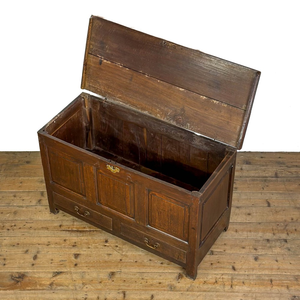 An 18th-century dark oak mule chest featuring three raised fielded panels, two lower drawers with brass swan-neck handles, and carved initial detailing. View V