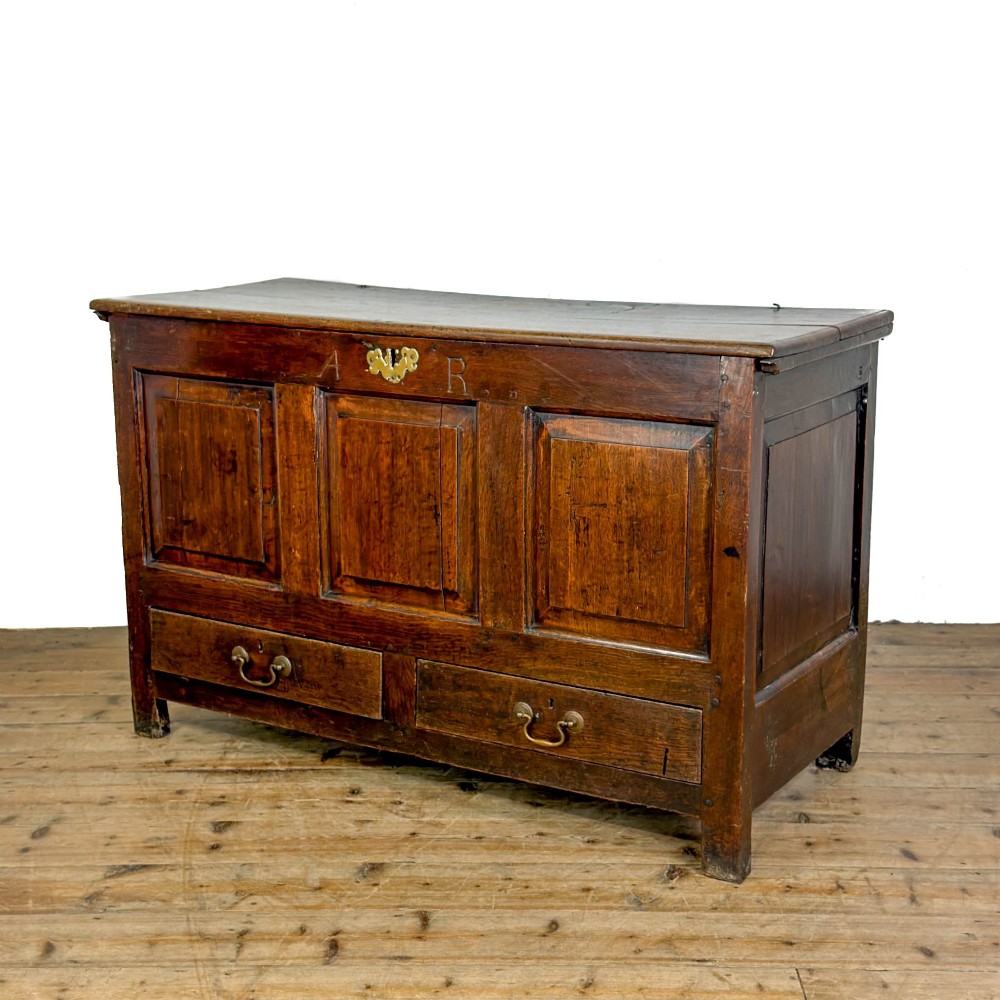 An 18th-century dark oak mule chest featuring three raised fielded panels, two lower drawers with brass swan-neck handles, and carved initial detailing. View VII