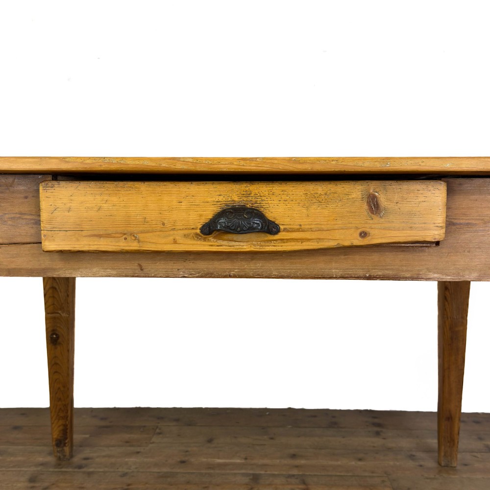An antique pine kitchen table featuring a plank top, a single apron drawer with a cast iron cup handle, and four tapered square legs. View III