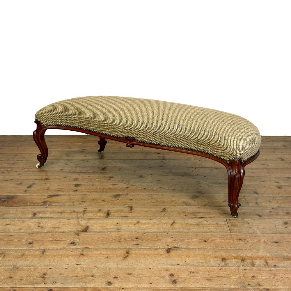 A long curved Victorian upholstered window seat featuring carved mahogany cabriole legs on castors and a patterned textile seat with studding detail.