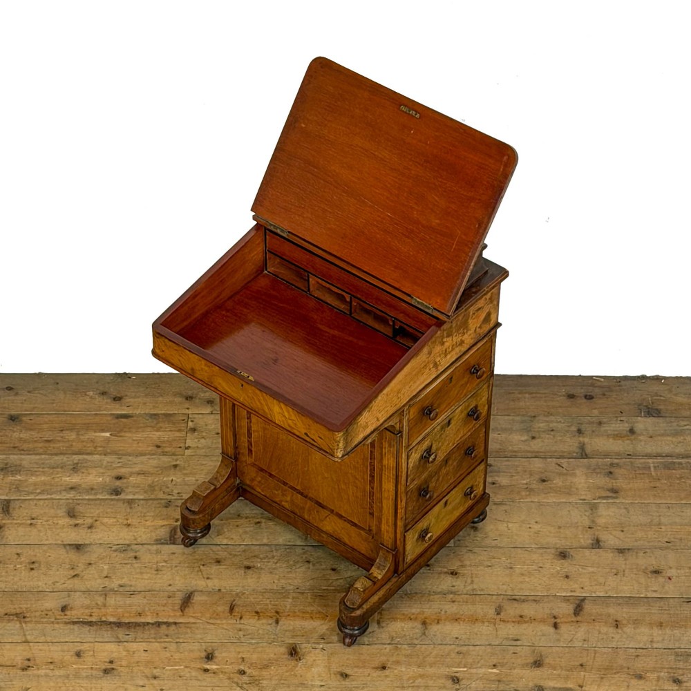 A Victorian burr walnut Davenport desk featuring a green leather writing slope, upper stationer compartment, side drawers, and brass castors. View VI