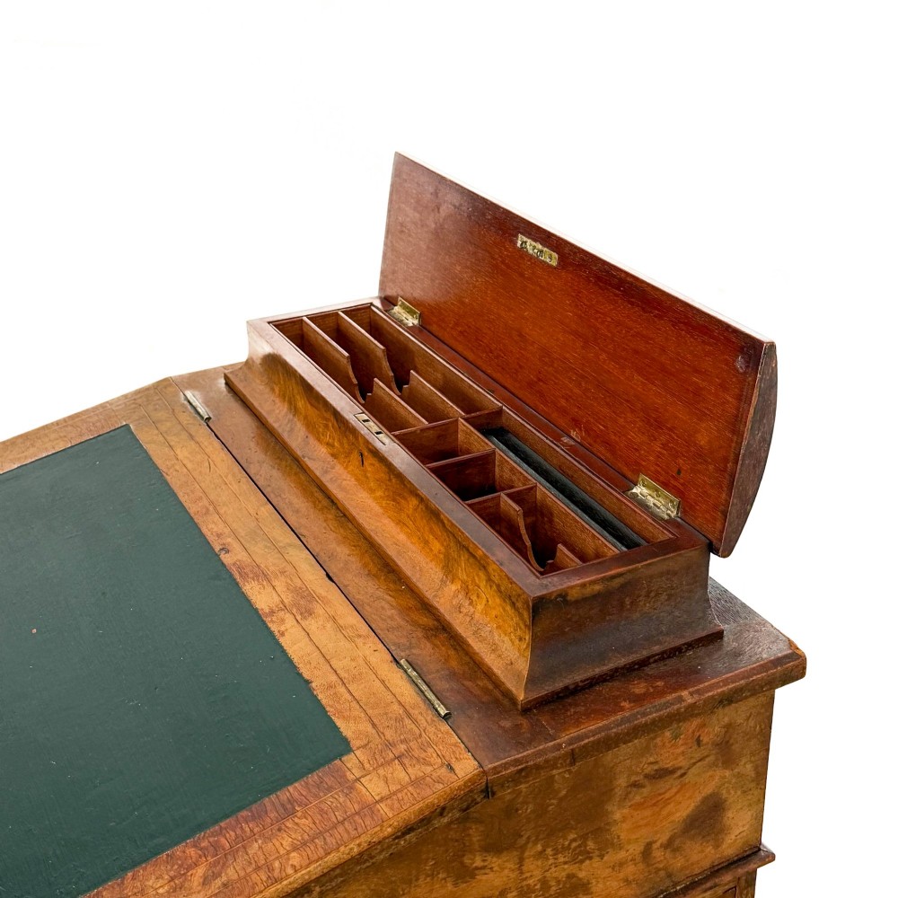 A Victorian burr walnut Davenport desk featuring a green leather writing slope, upper stationer compartment, side drawers, and brass castors. View IX
