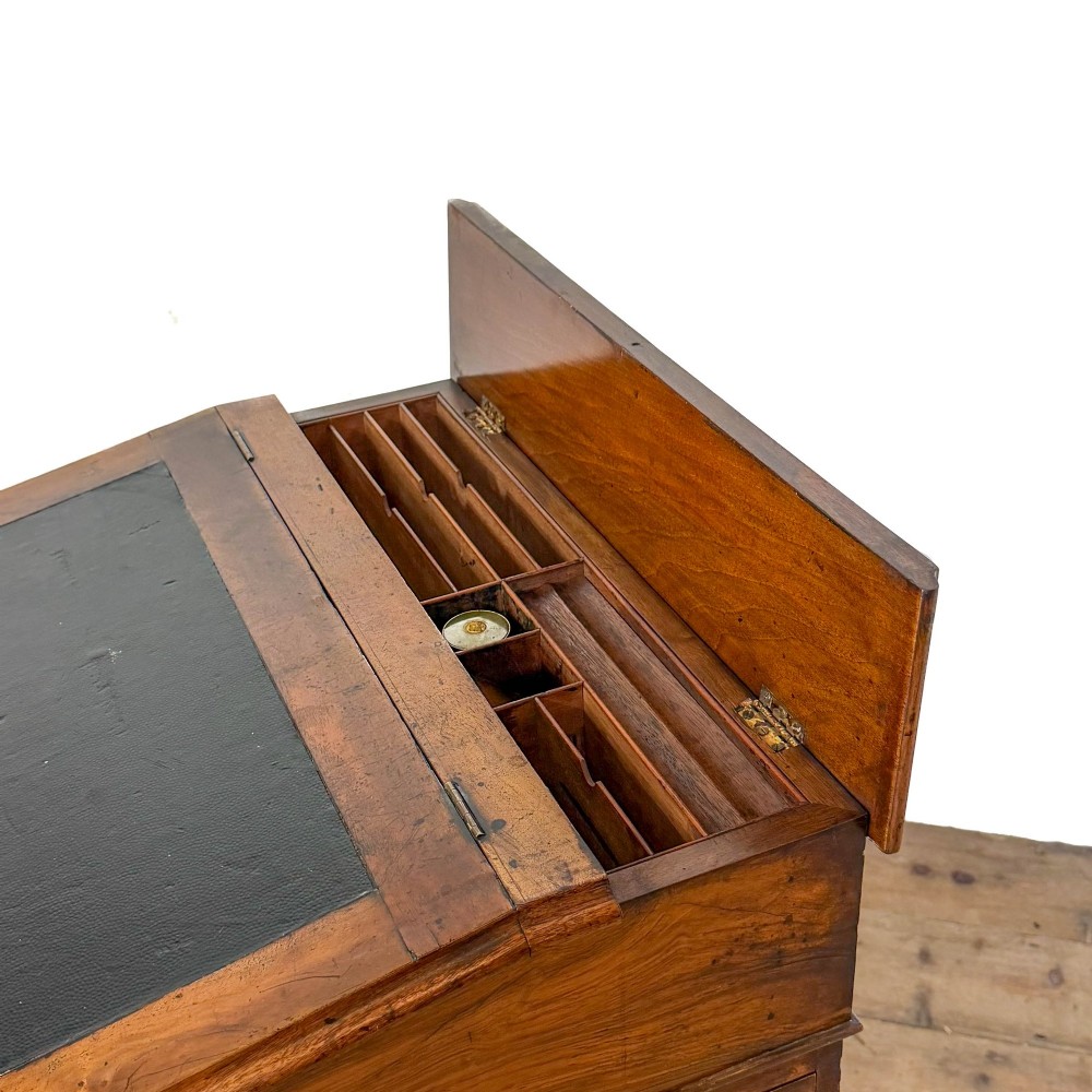 A Victorian walnut davenport desk featuring a slanted dark leather writing surface, carved front scroll supports, side drawers, and brass castors. View II