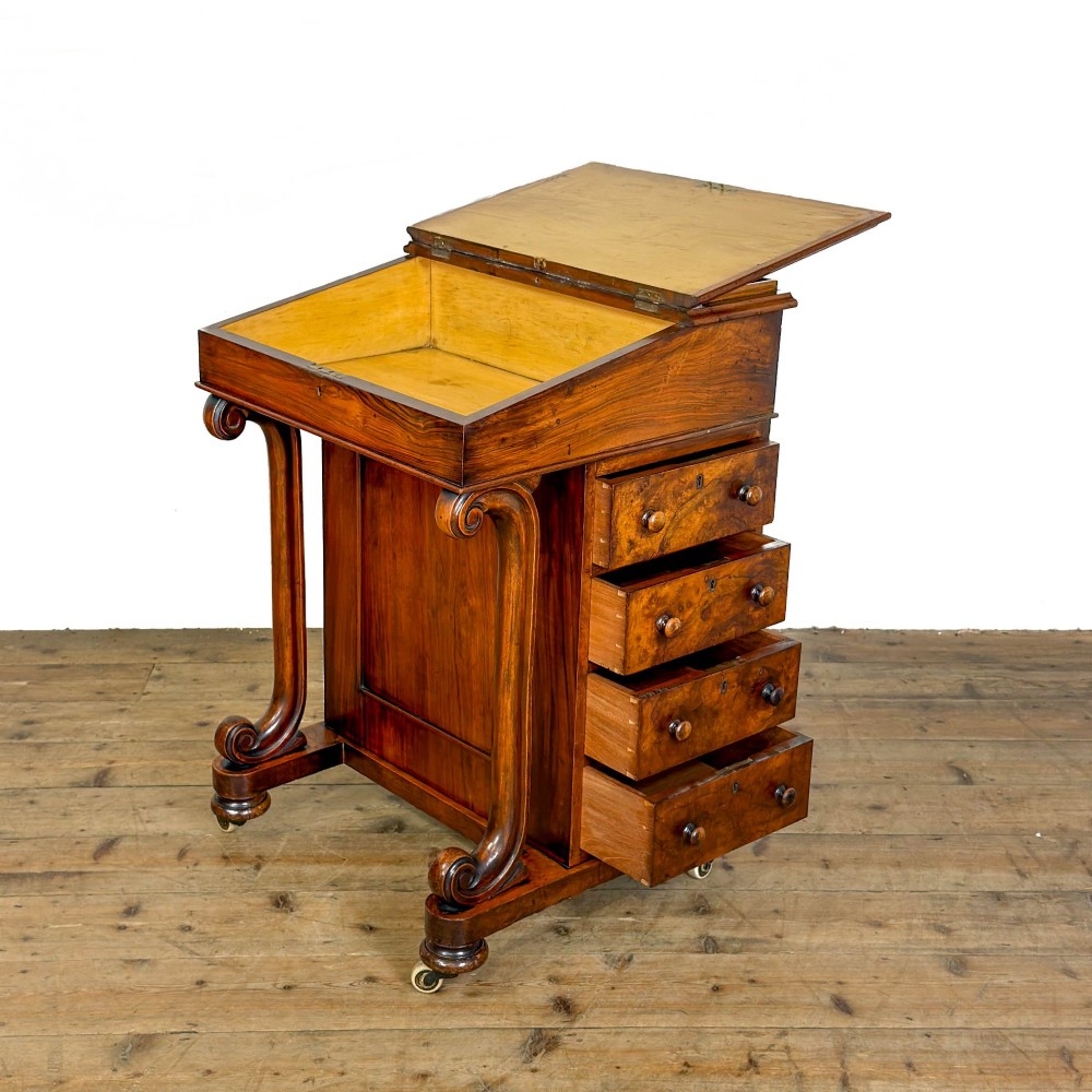 A Victorian walnut davenport desk featuring a slanted dark leather writing surface, carved front scroll supports, side drawers, and brass castors. View IV