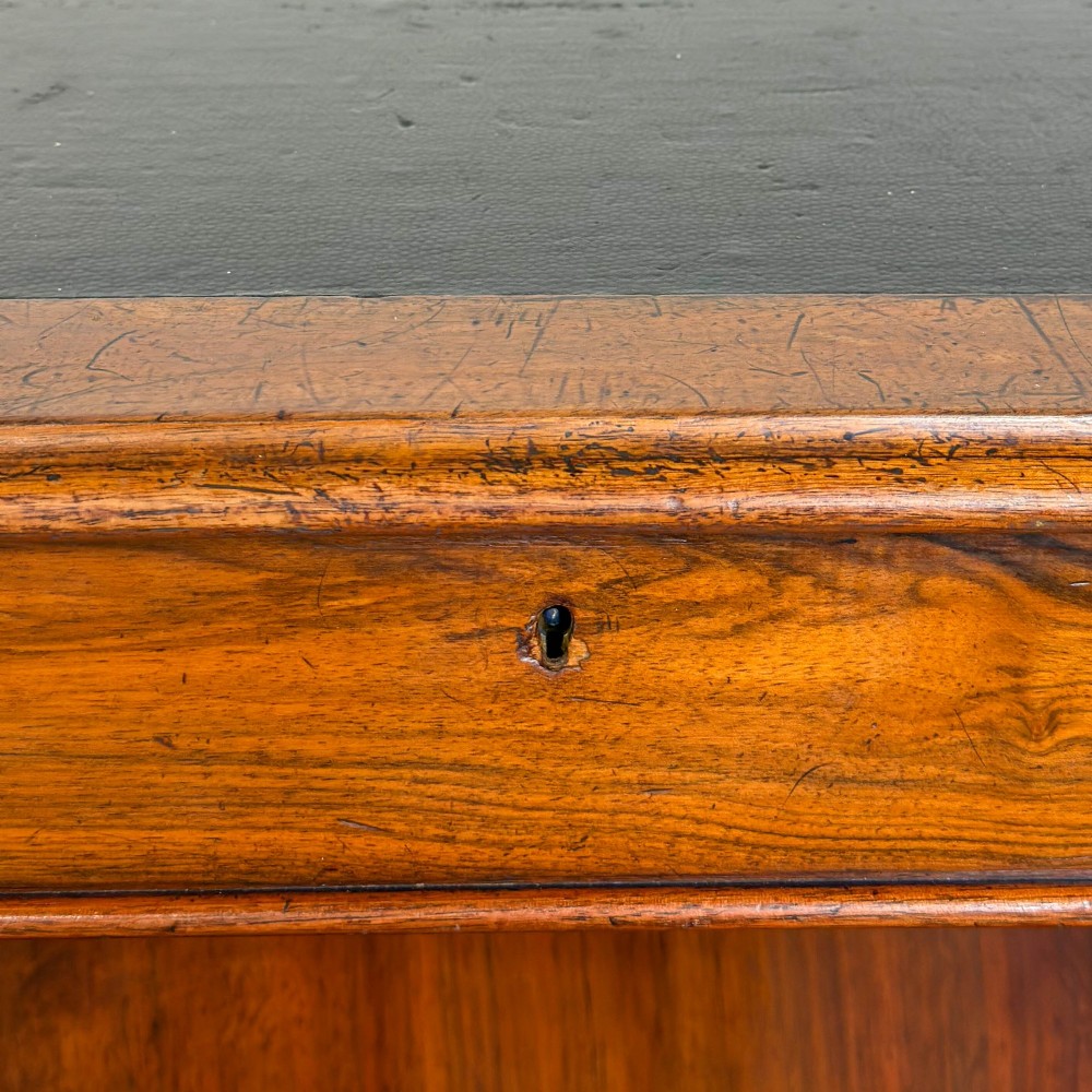 A Victorian walnut davenport desk featuring a slanted dark leather writing surface, carved front scroll supports, side drawers, and brass castors. View VI