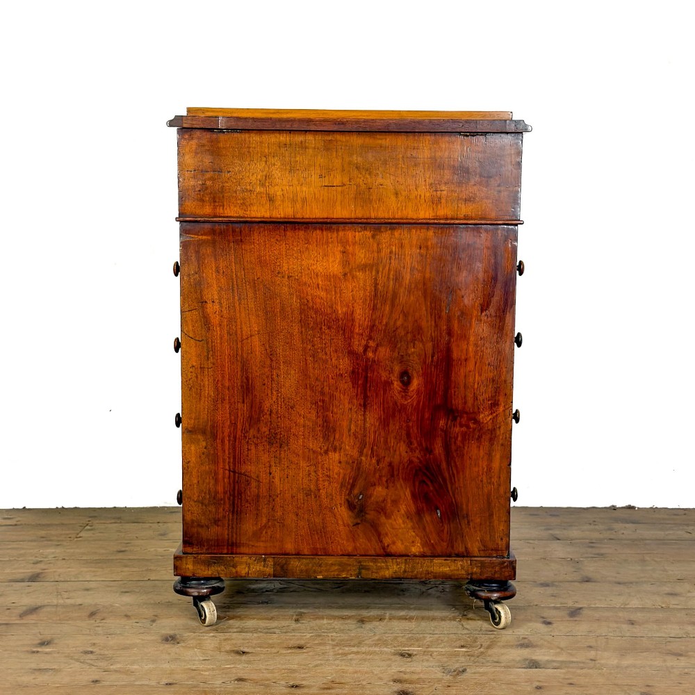 A Victorian walnut davenport desk featuring a slanted dark leather writing surface, carved front scroll supports, side drawers, and brass castors. View VIII