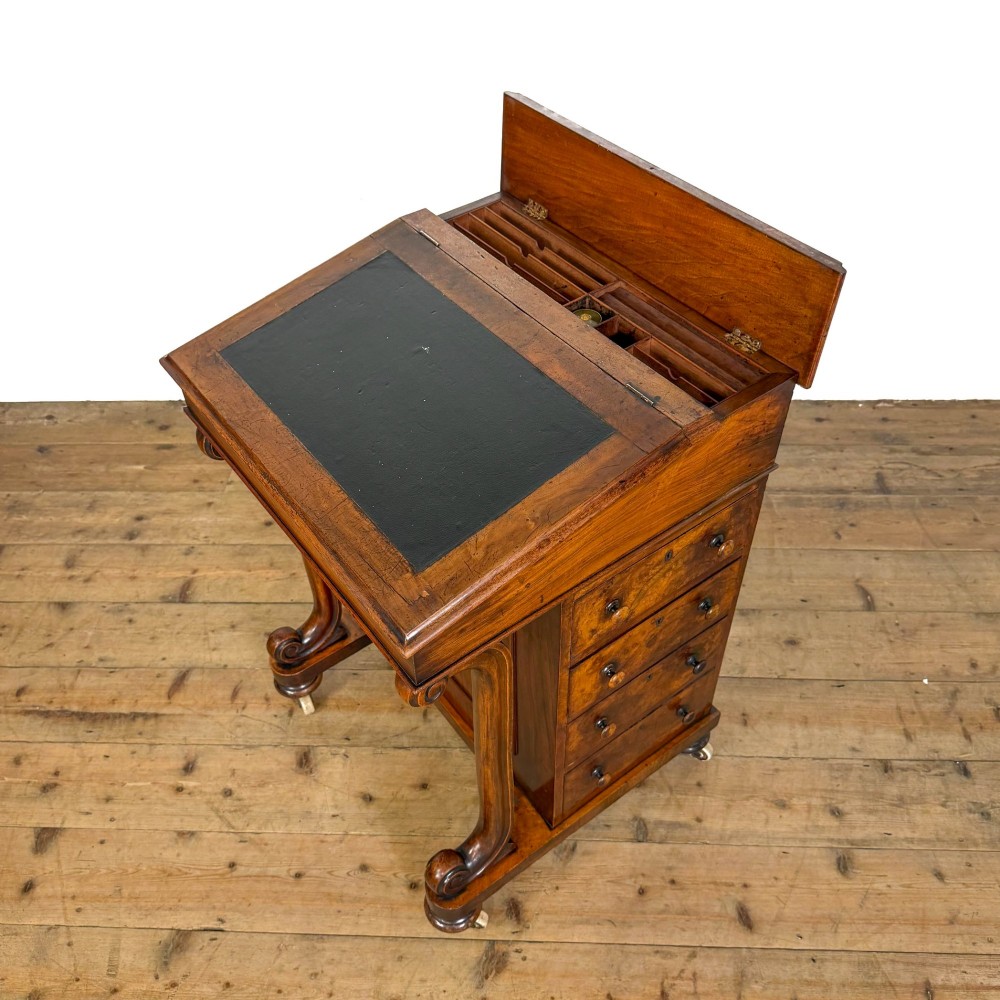 A Victorian walnut davenport desk featuring a slanted dark leather writing surface, carved front scroll supports, side drawers, and brass castors. View XI