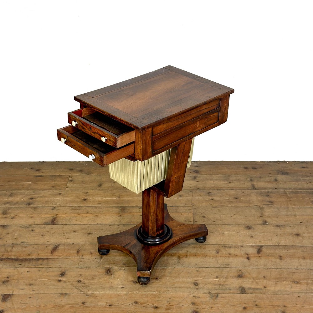 A 19th-century rosewood work table featuring small drawers, a pleated cream fabric basket underneath, a central pedestal support, and a quadruped base. View V