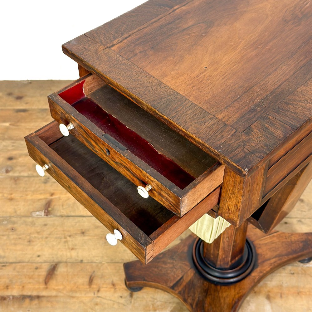 A 19th-century rosewood work table featuring small drawers, a pleated cream fabric basket underneath, a central pedestal support, and a quadruped base. View VI