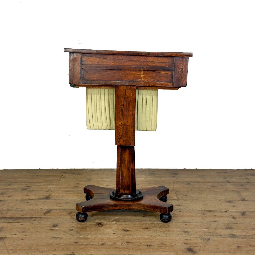 A 19th-century rosewood work table featuring small drawers, a pleated cream fabric basket underneath, a central pedestal support, and a quadruped base. View VII